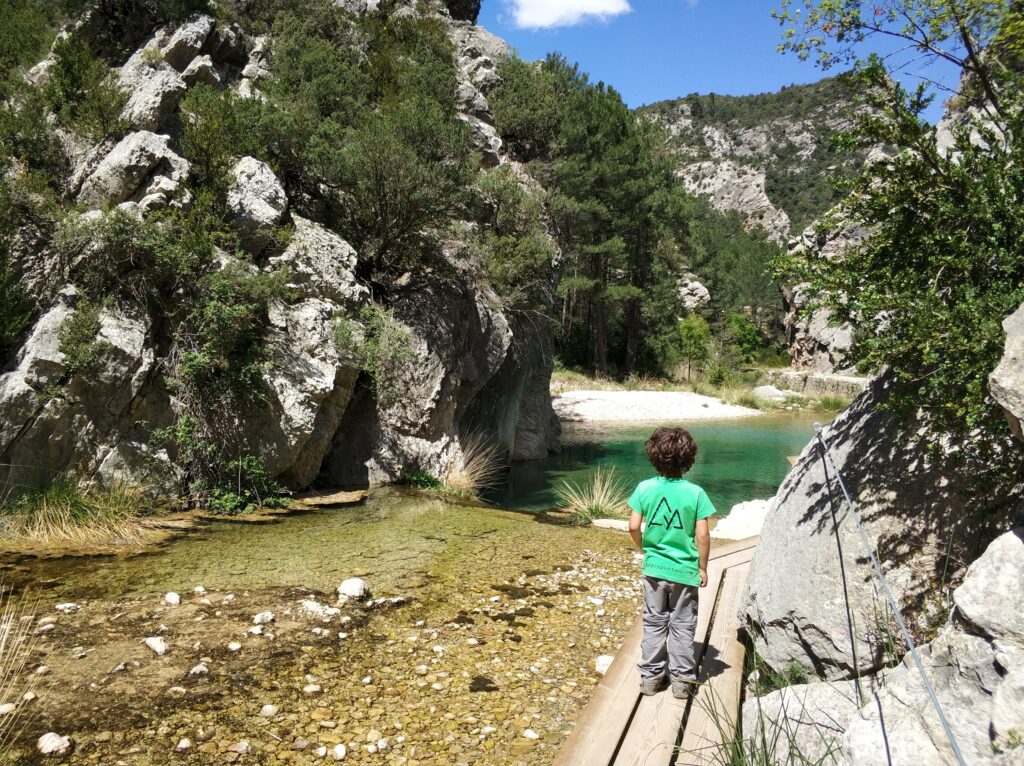 Niño en la pasarela del Parrizal de Beceite junto a una poza de agua turquesa, Els Ports, Teruel