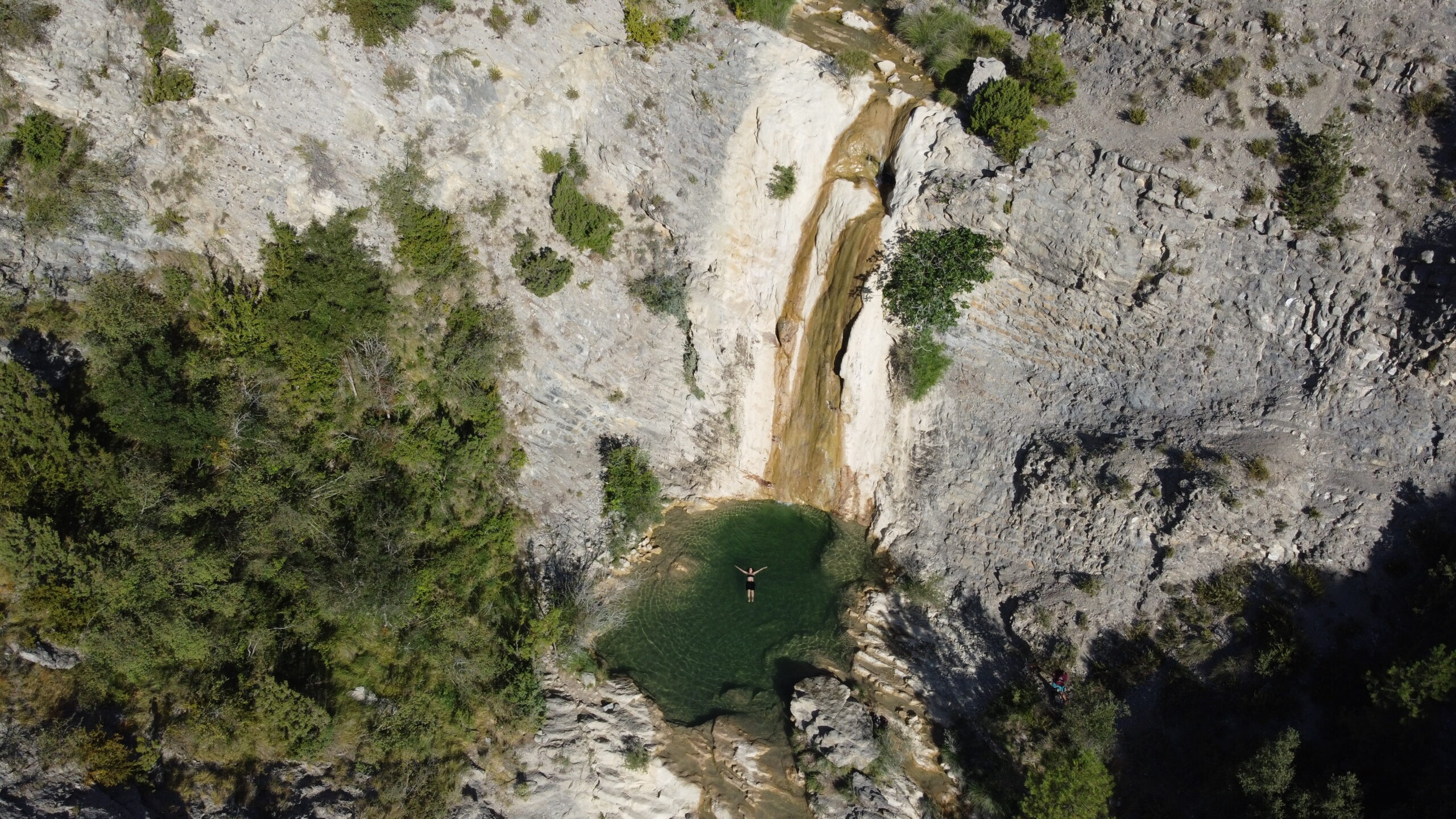 Persona flotando en la poza verde de las cascadas de Organyà vista desde arriba