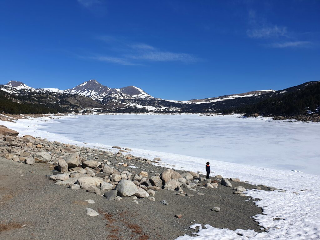 Niño a los pies de un lago cubierto de nieve en el pirineo